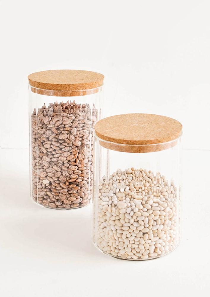 Two horizontally ribbed glass jars filled with beans and lidded with cork.