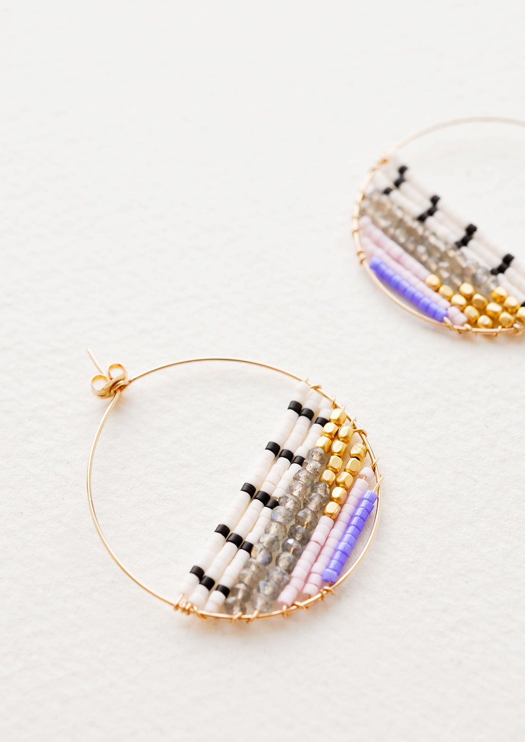 2: Close up of delicate gold hoop with multi-colored beads filling bottom half of hoop. 