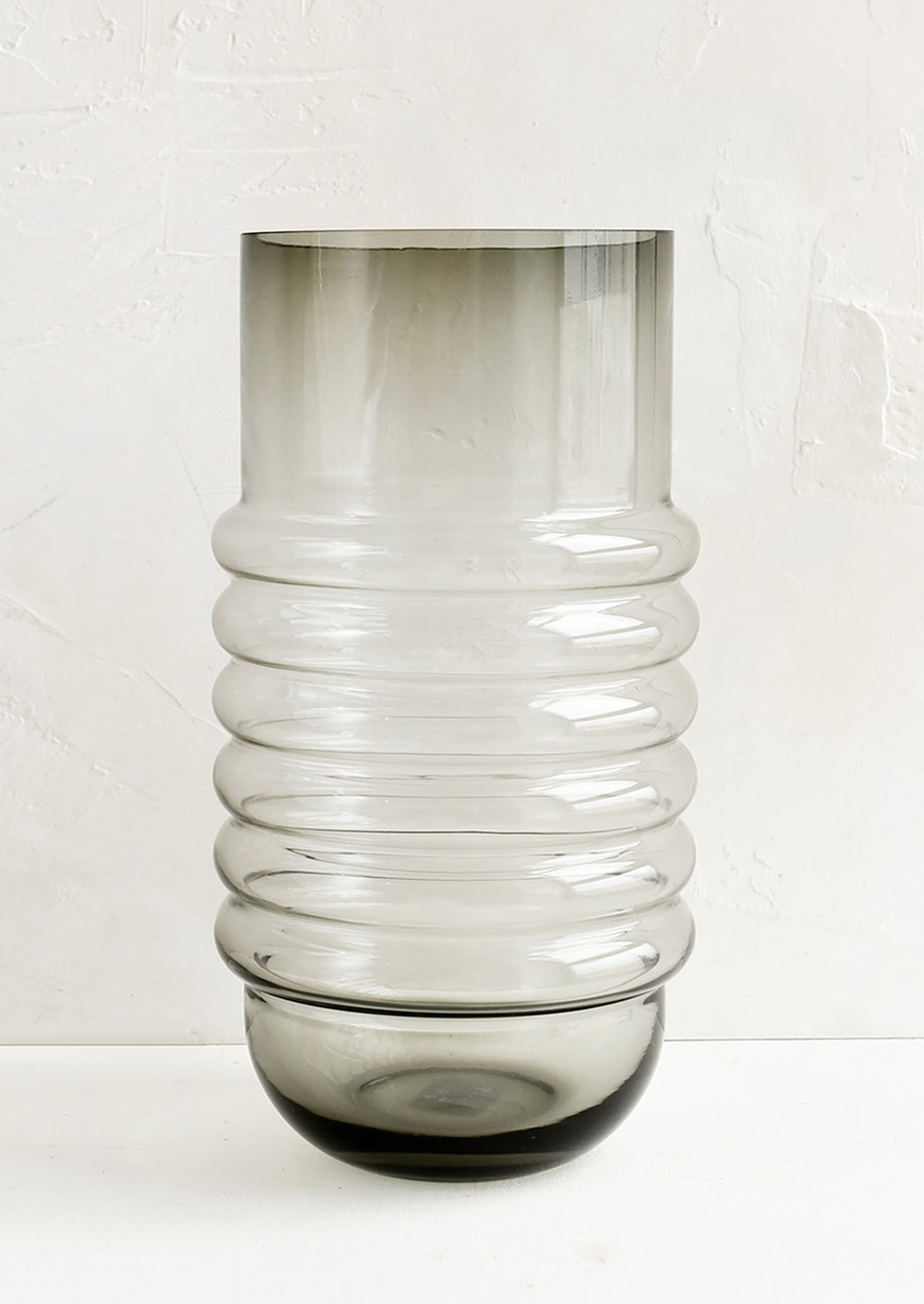 1: A tall grey glass vase with curved ribbing at middle.