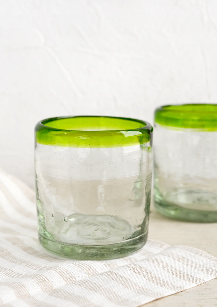 A heavy rocks glass in natural glass with colored green rim around top.