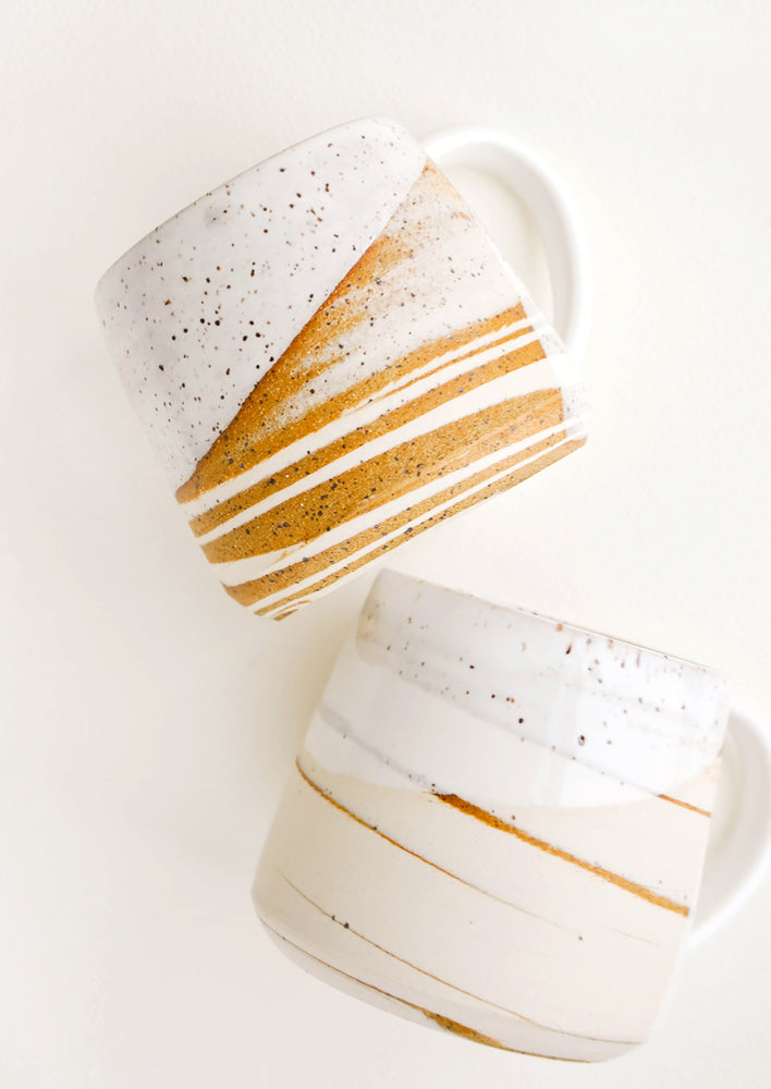 Two ceramic mugs with handles in swirled ivory and brown clay with speckled white glazed rim.
