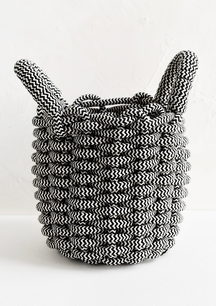 A black and white woven rope basket with top handles.