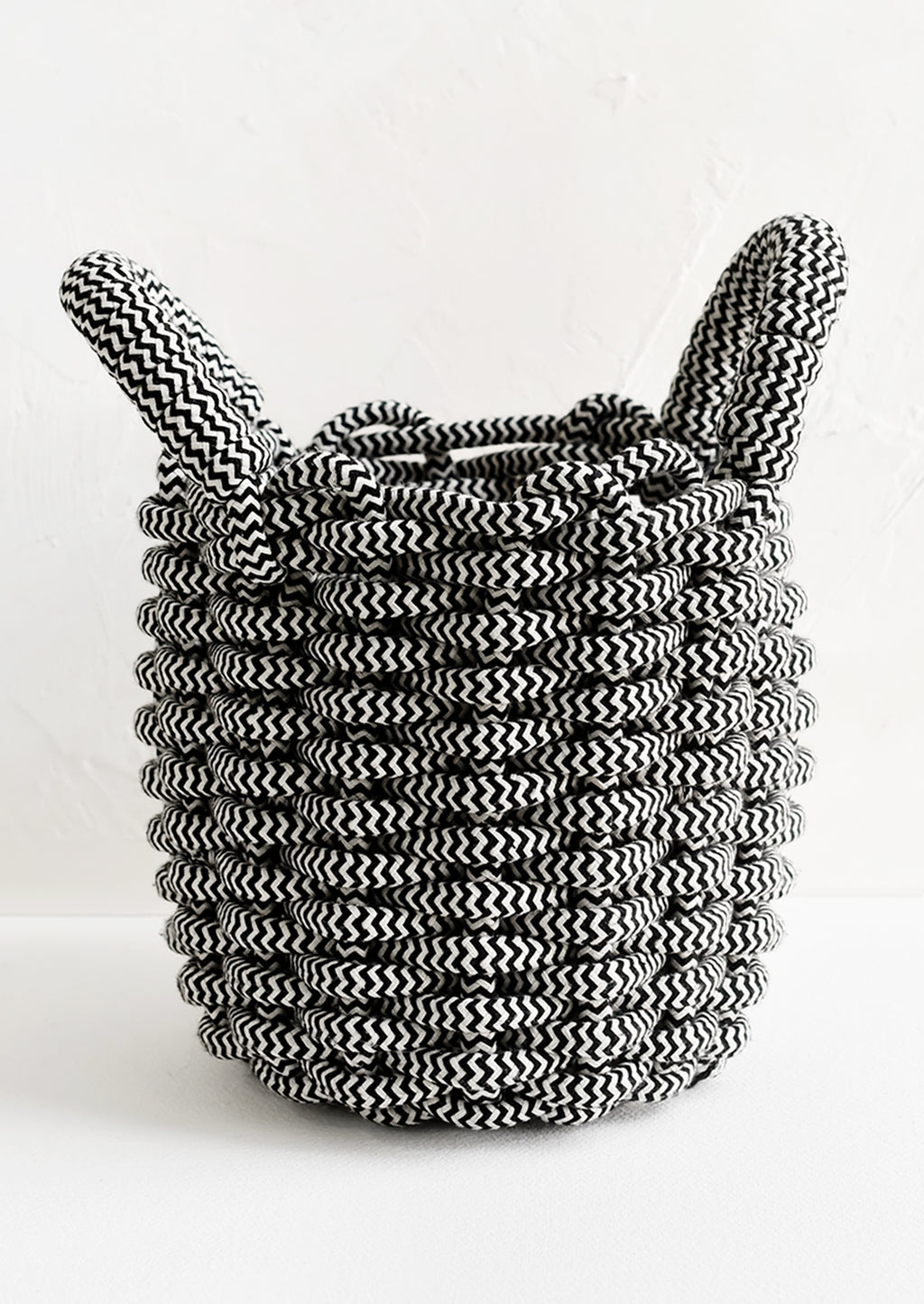 1: A black and white woven rope basket with top handles.