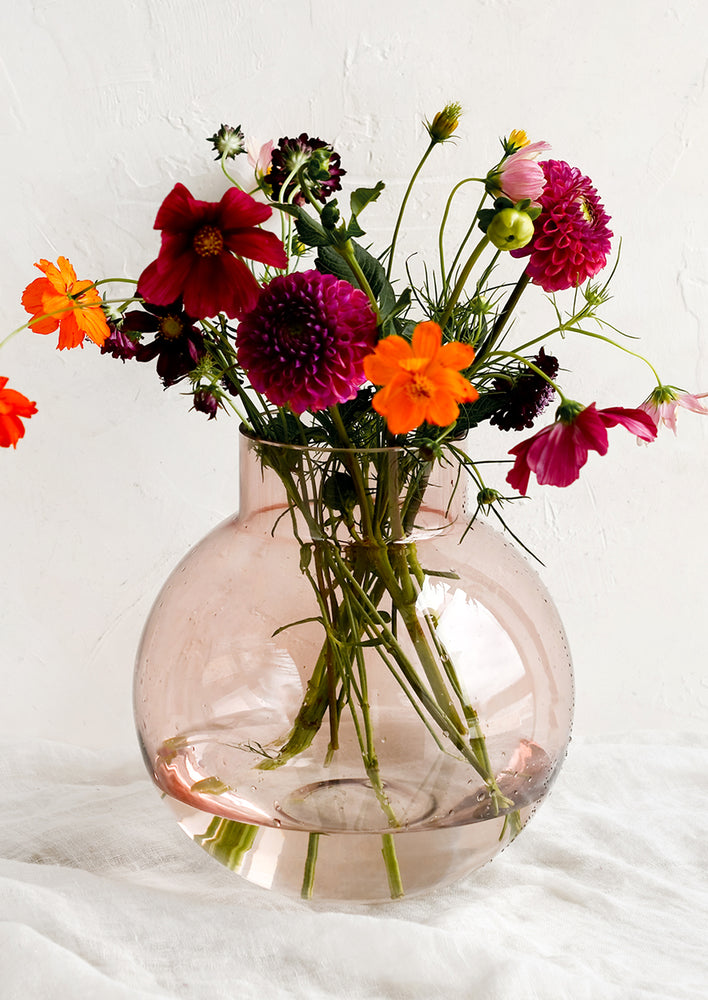 1: A round shaped glass vase in transparent pink, holding fresh flowers.