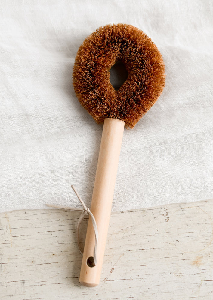 A kitchen brush with looped circular brush shape made from coconut fiber.