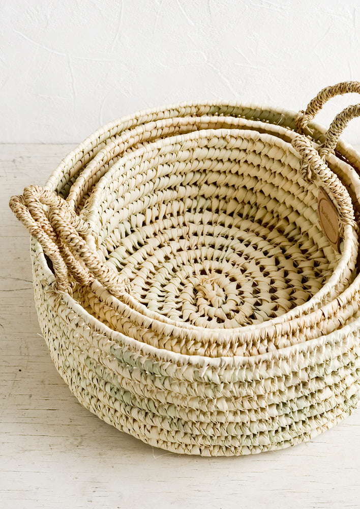 Three round palm leaf storage baskets in incremental sizes nested together.