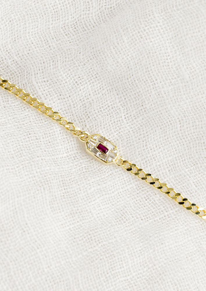 A gold chainlink bracelet with baguette ruby and crystal charm.
