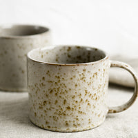 2: A brown speckled coffee mug with round handle.