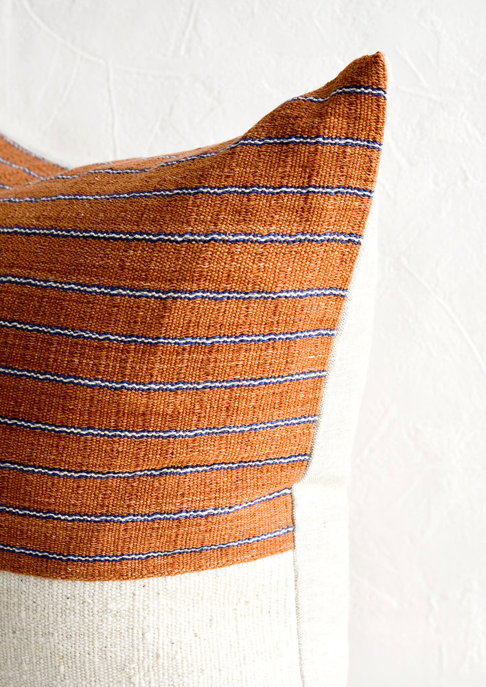 3: A throw pillow with top half in rust & indigo striped fabric and natural linen back.