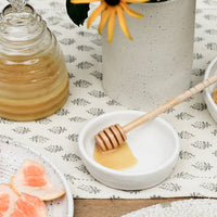 2: A table setting with honey jar and honey dipper in bowl.