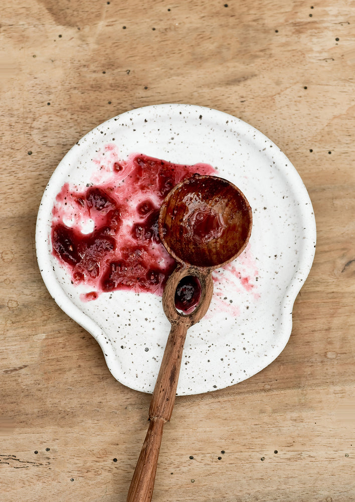 2: A wooden spoon with raspberry jam on ceramic spoon rest.