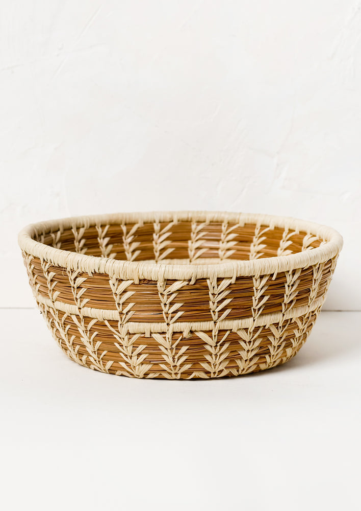 A woven catchall basket in bowl shape made from pine needles and raffia.