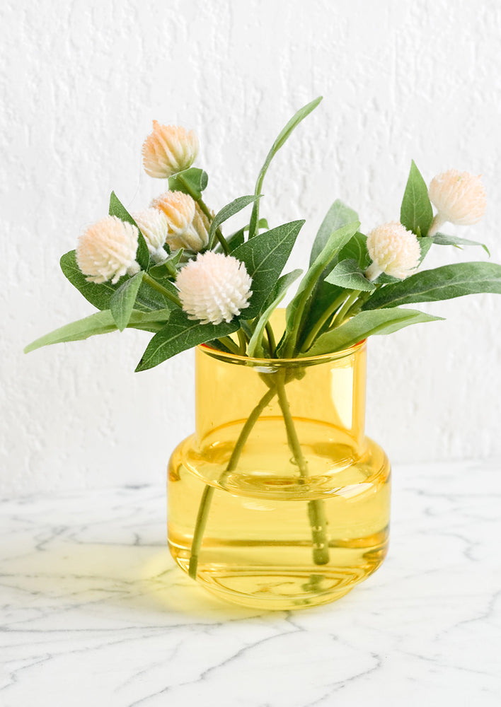 A small yellow glass vase with gomphrena flowers.
