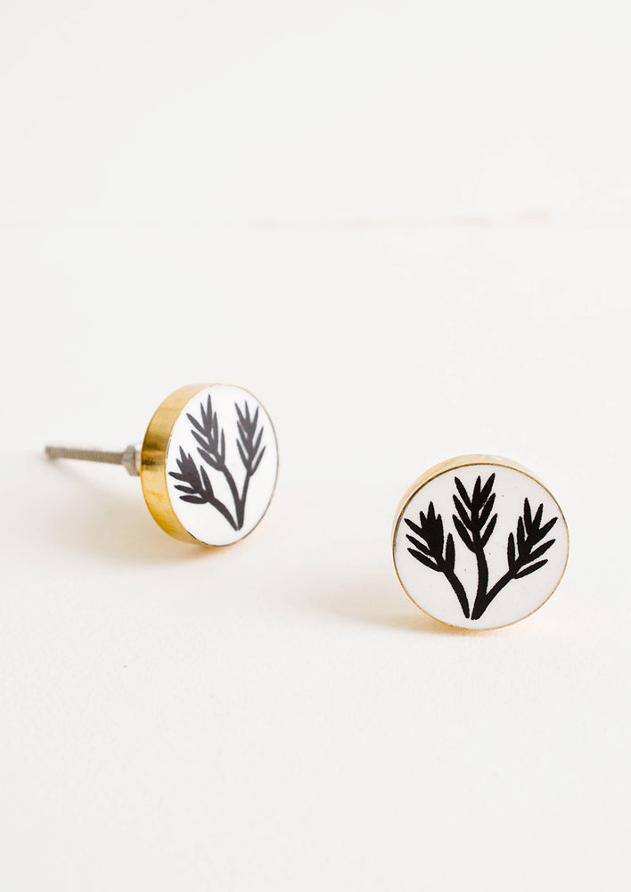 Round drawer knobs with white background and black leaf print, surrounded by brass bezel