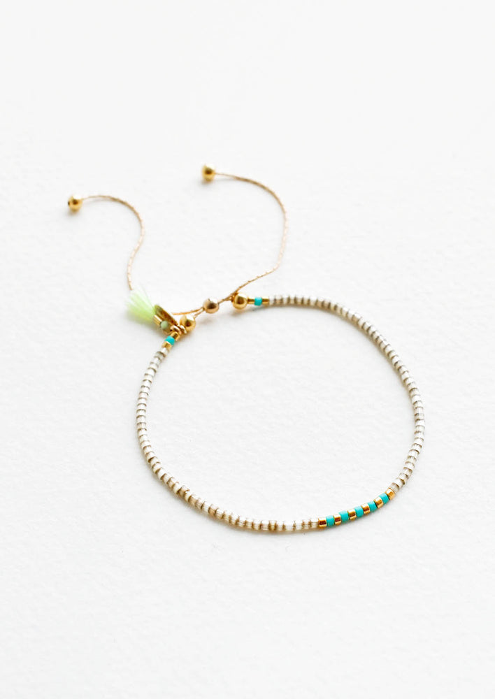 Delicate bracelet of gray glass beads with alternating turquoise and gold beads at center on a thin gold chain.