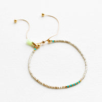 Khaki / Turquoise: Delicate bracelet of gray glass beads with alternating turquoise and gold beads at center on a thin gold chain.