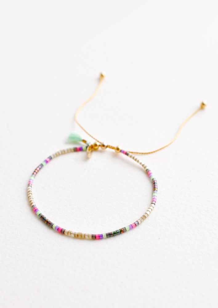 Delicate bracelet of gray glass beads with regularly spaced sections of pink and green beads on a thin gold chain.