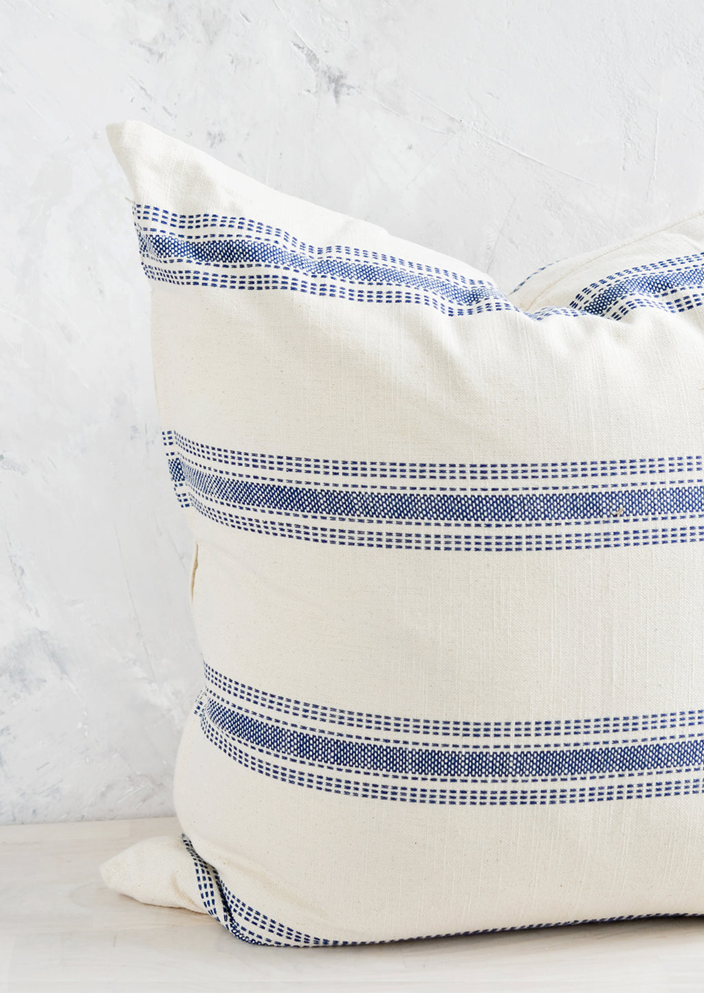 2: A large, square-shaped throw pillow in cream cotton with horizontal embroidered blue stripes.