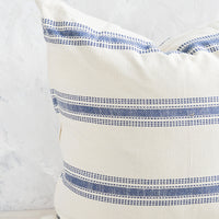 2: A large, square-shaped throw pillow in cream cotton with horizontal embroidered blue stripes.