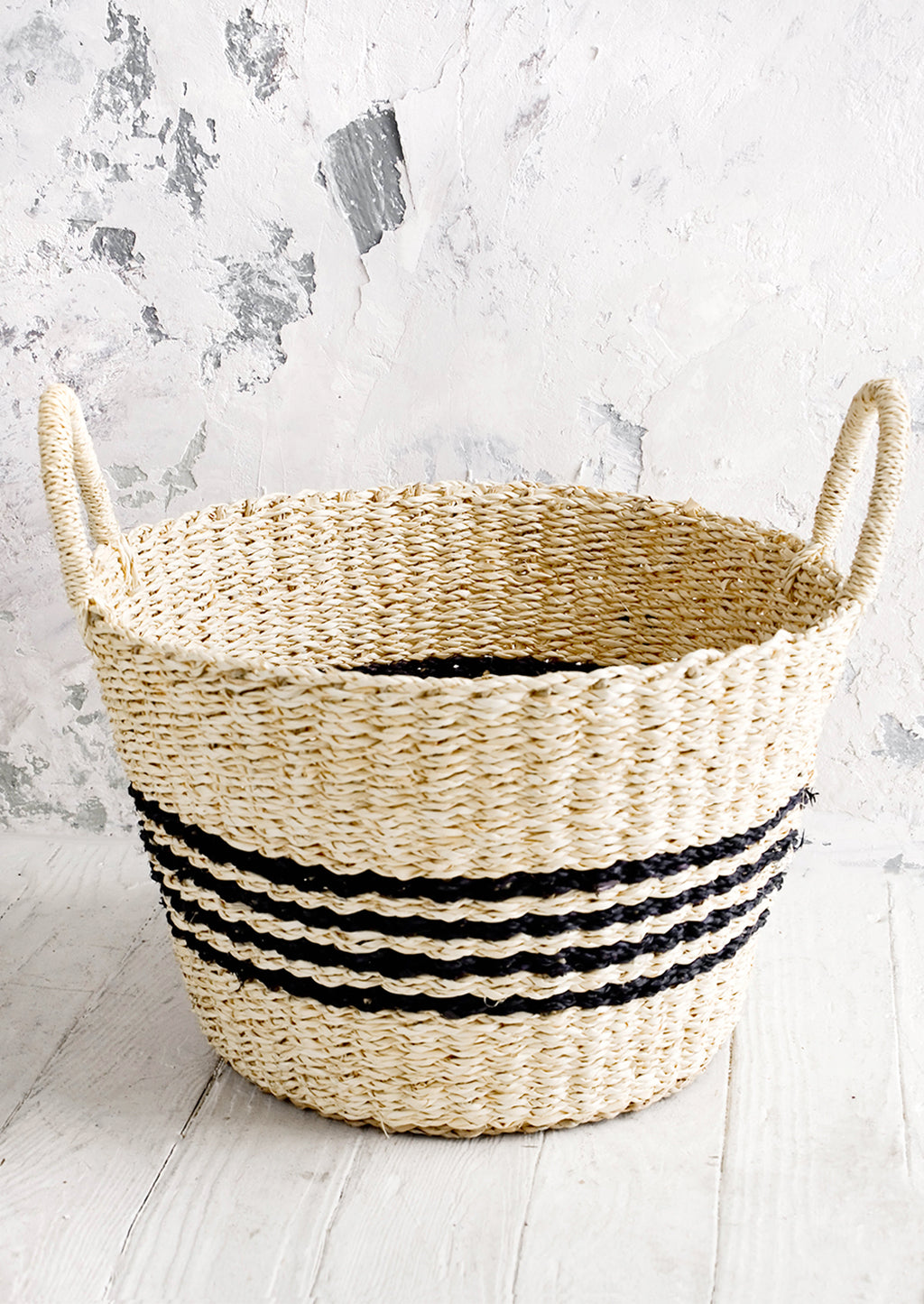 1: Round woven storage basket with thin black stripes, tapered bottom and two handles.