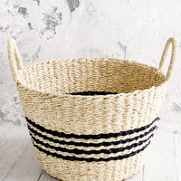 1: Round woven storage basket with thin black stripes, tapered bottom and two handles.