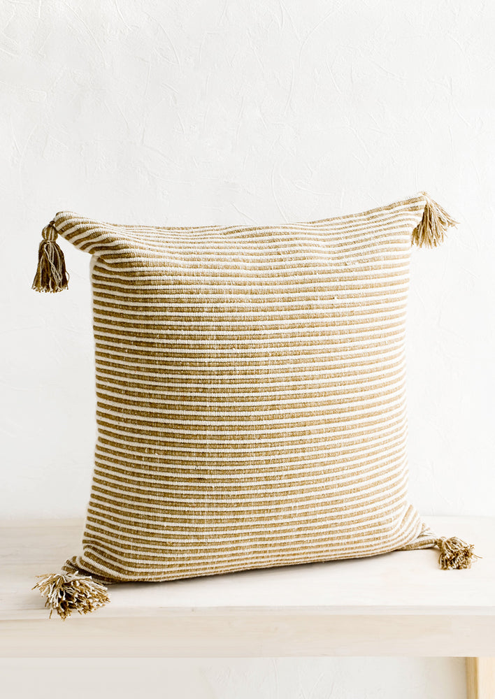 Large square throw pillow in textured light brown and cream stripes, decorative tassel at each corner