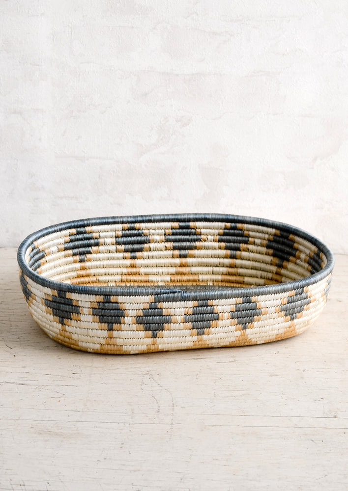 An oval shaped basket made from woven sweetgrass in dusty blue and tan geometric pattern.