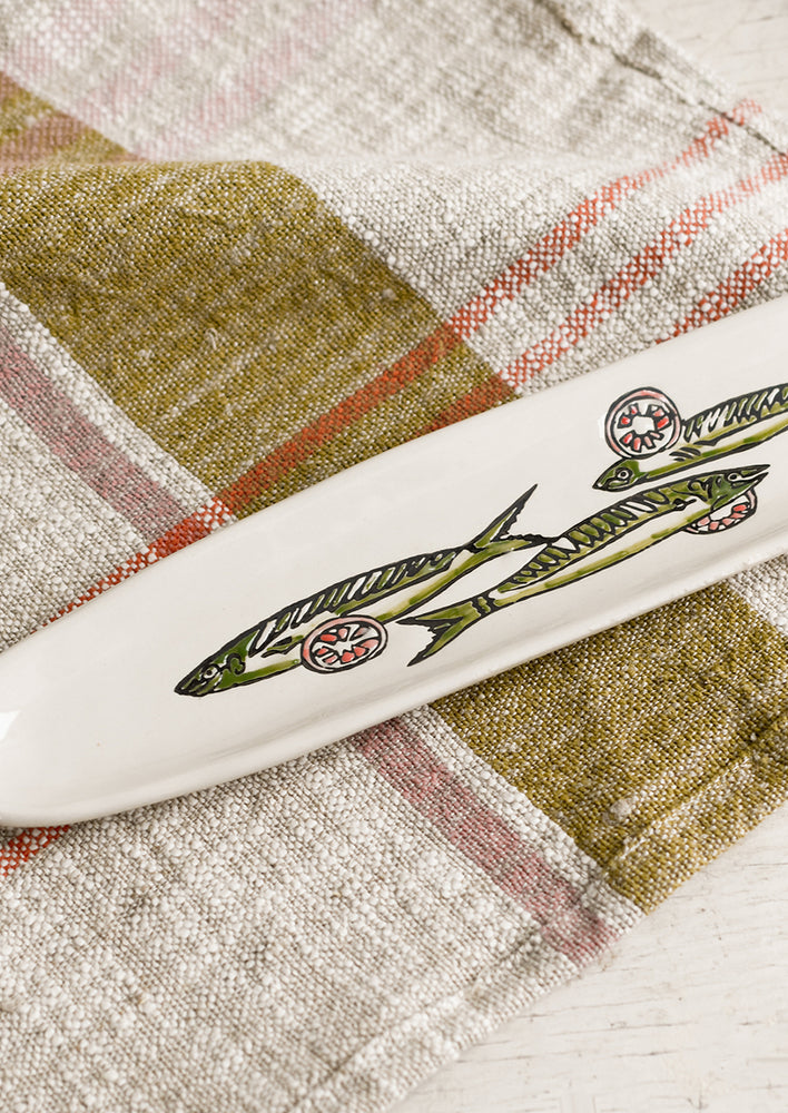 2: A long and skinny white ceramic dish with green sardine print.