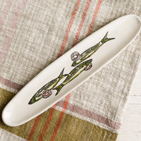 1: A long and skinny white ceramic dish with green sardine print.