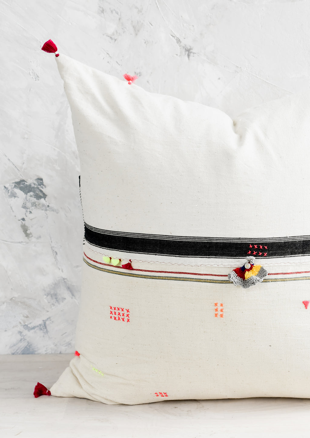 2: A square throw pillow with neon embroidery and tassel detailing.