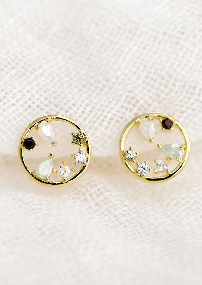 A pair of gold circular stud earrings with a mix of color and shape crystals inside the circle.