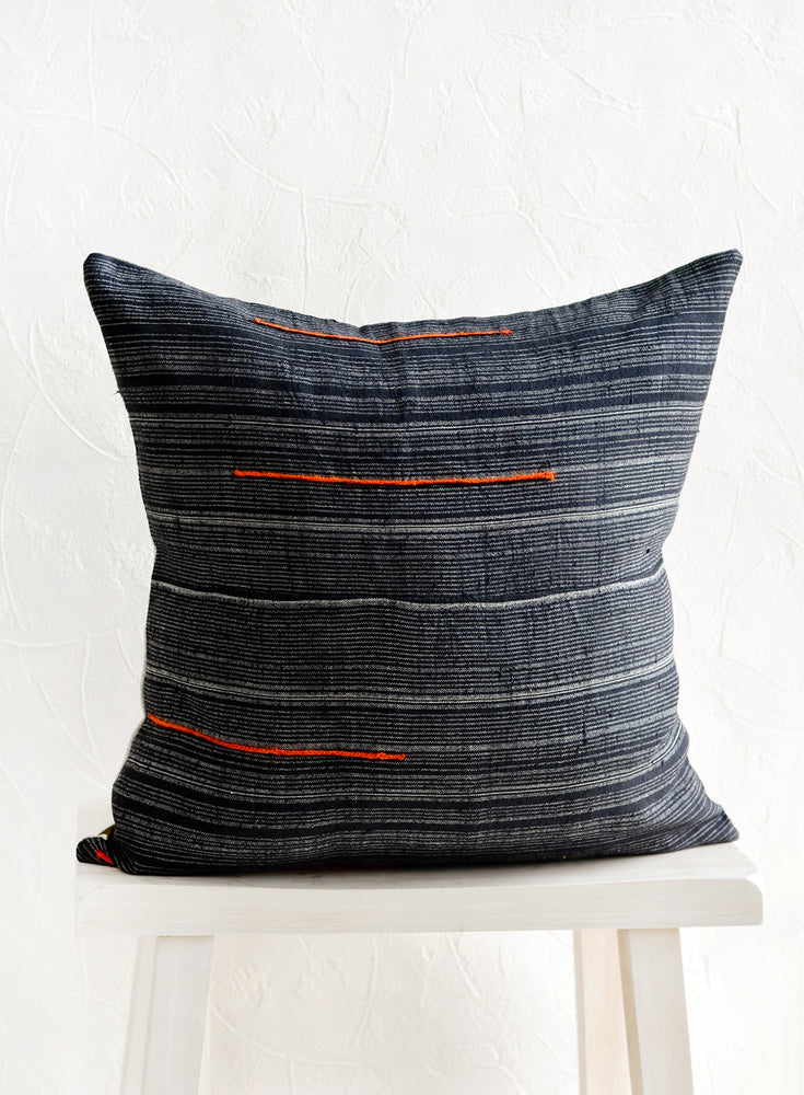 2: A square throw pillow made from dark blue fabric with grey stripes and embroidered orange lines.