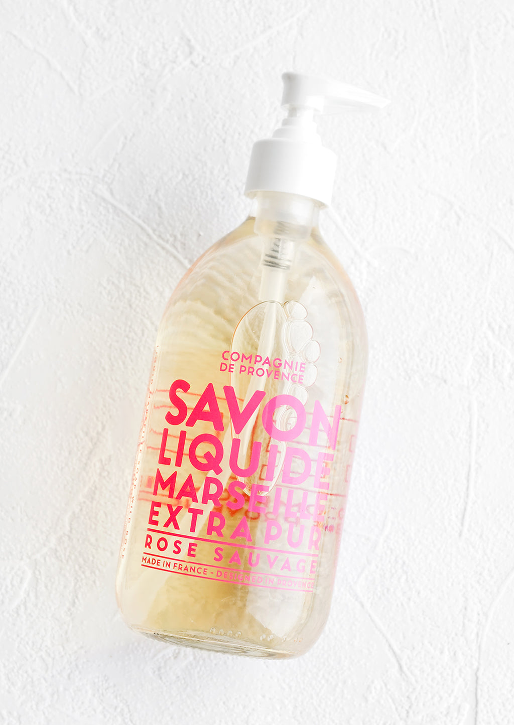 Wild Rose: A clear glass soap bottle with bold pink text printed on bottle