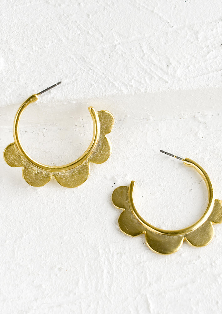 A pair of gold hoop earrings with scalloped trim.