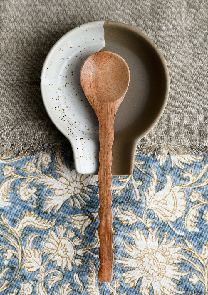 A wooden spoon on a ceramic spoon rest.