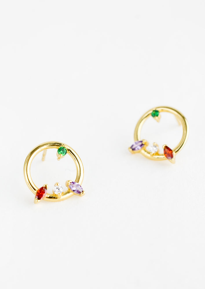 2: A pair of gold stud earrings in the shape of a circle with randomized colored crystal detailing.