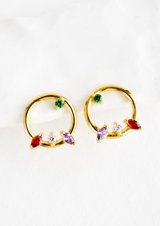 A pair of gold stud earrings in the shape of a circle with randomized colored crystal detailing.