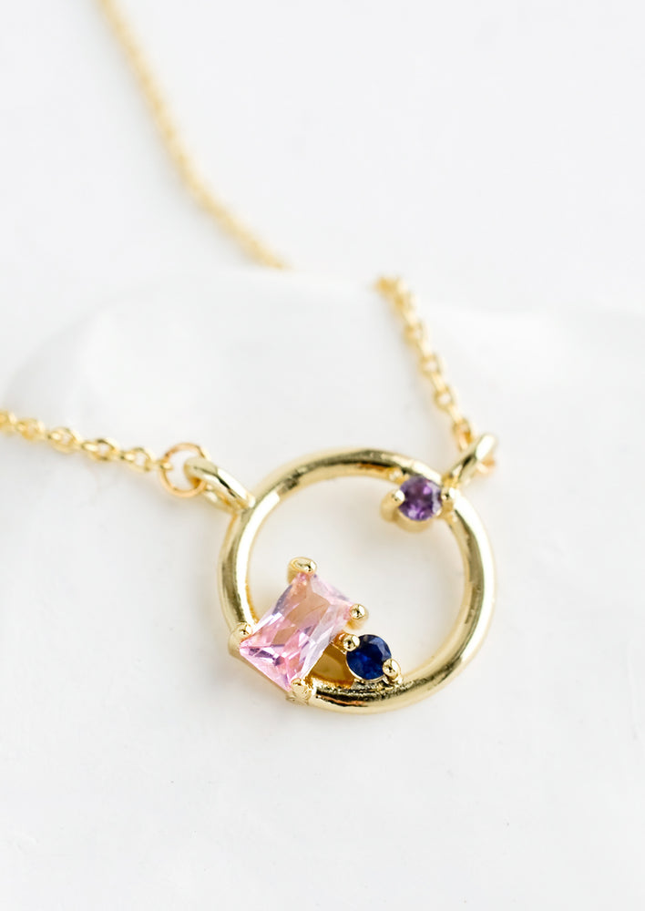 A gold necklace with delicate chain and circular charm with colored crystal detail.