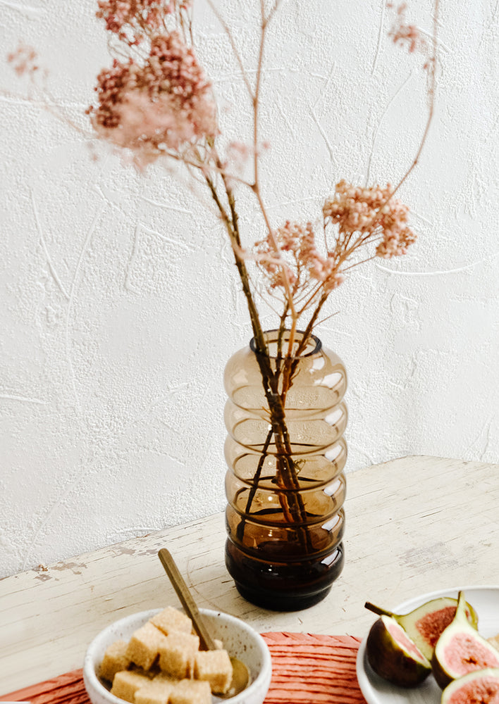 2: A clear brown glass vase in a curvy silhouette with dried pink flowers.