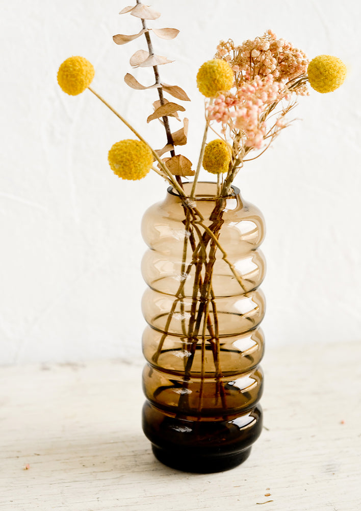A clear brown glass vase in a curvy silhouette with pink and yellow flowers.