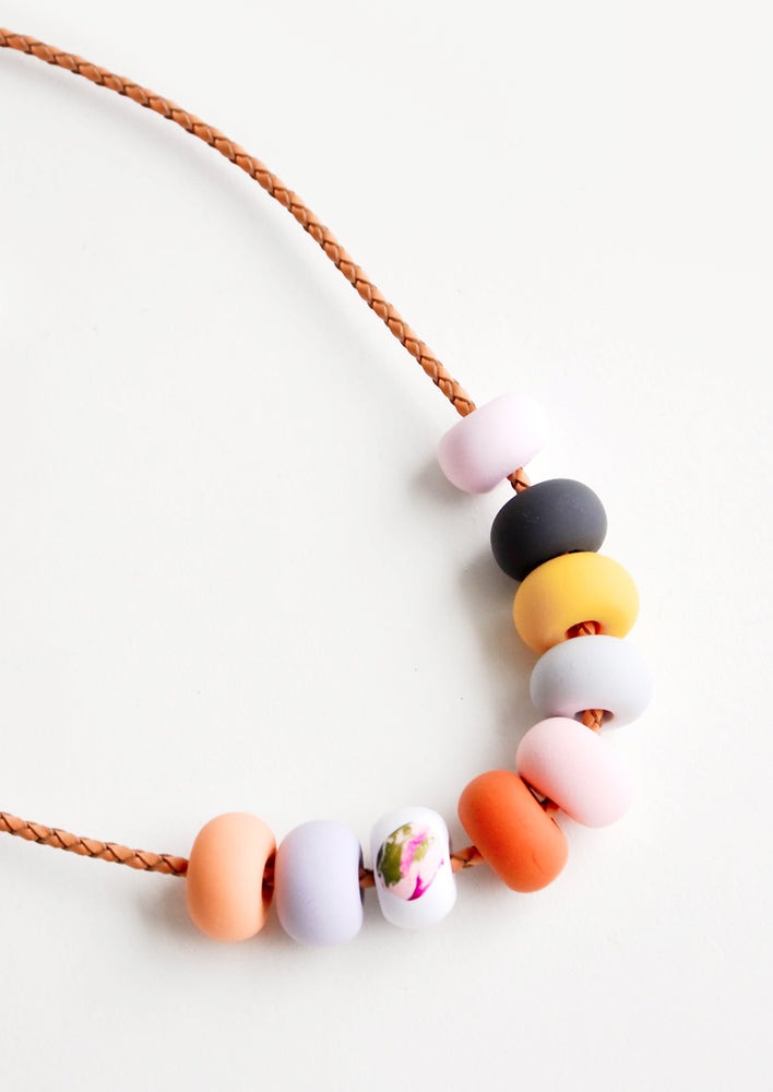 Close up of necklace with nine rounded clay beads in pink, navy, yellow, red, and orange.