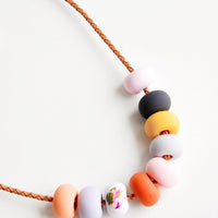3: Close up of necklace with nine rounded clay beads in pink, navy, yellow, red, and orange.