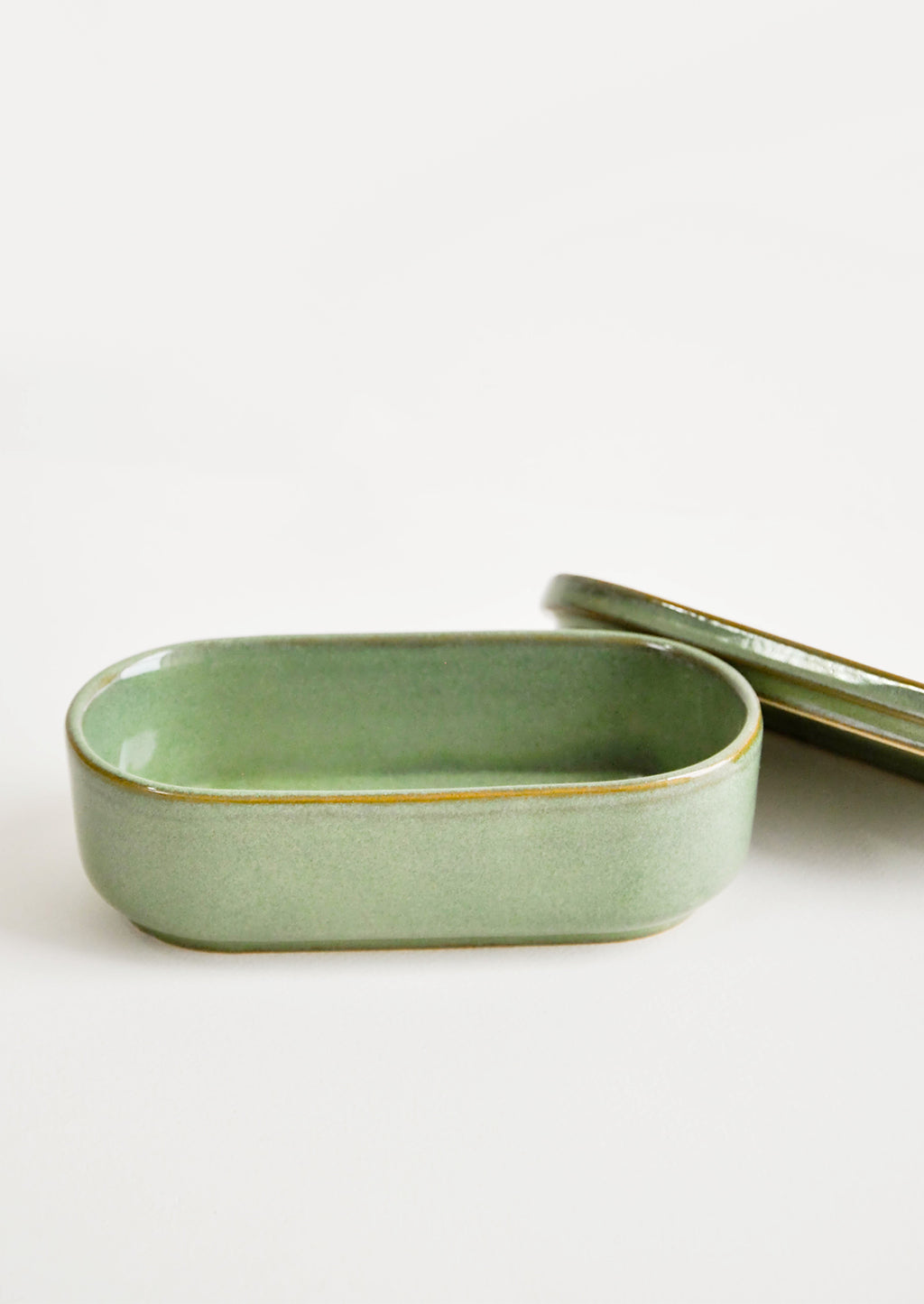 2: Oblong oval ceramic green Container with lid lying by its side.
