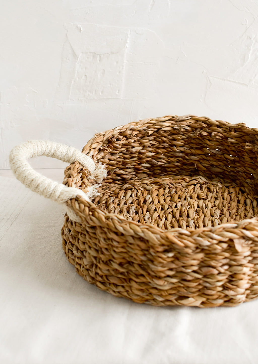 1: A round, shallow tray made from seagrass with ivory jute handles at sides.