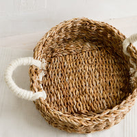 2: A round, shallow tray made from seagrass with ivory jute handles at sides.