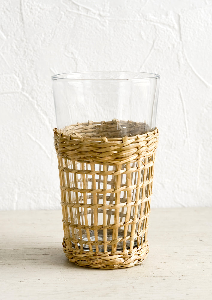 A tall glass cup wrapped in decorative seagrass cage.