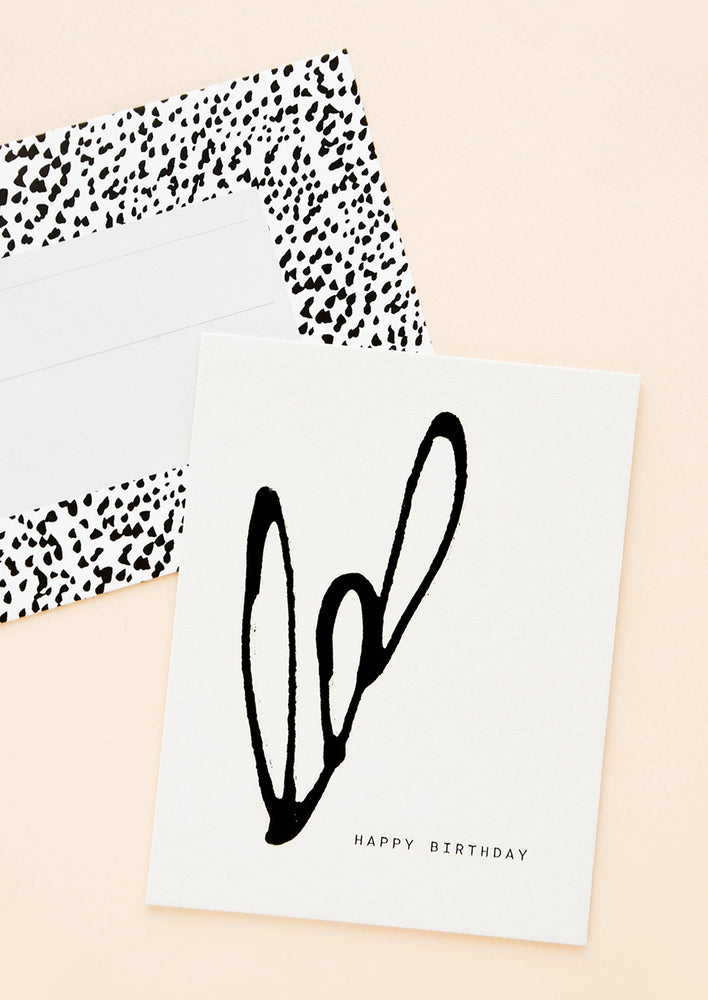 A black and white dotted envelope and white greeting card reading "happy birthday" with a simple organic design in black paint.