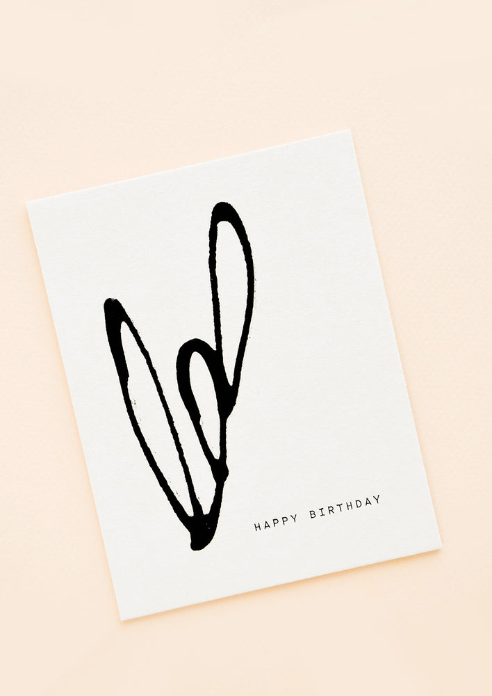 A white greeting card reading "happy birthday" with a simple organic design in black paint.