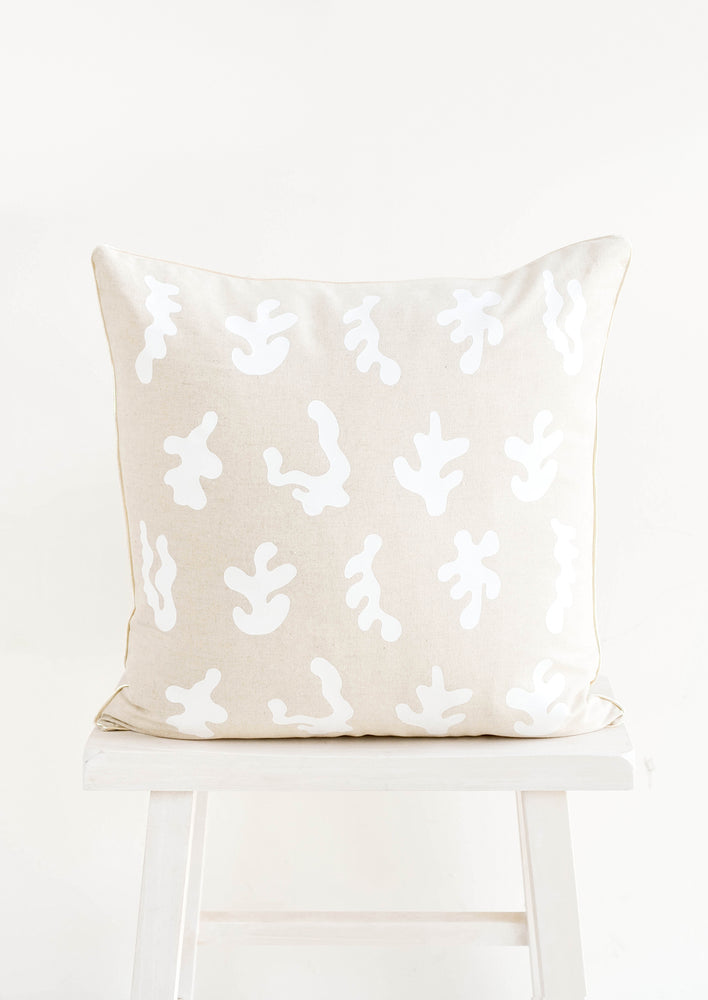 Square throw pillow in natural linen color with white, screen printed seaweed shapes 
