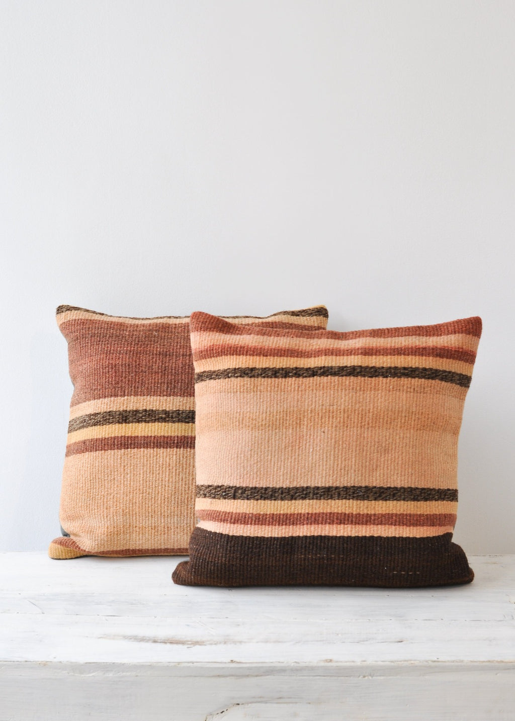 2: Two square kilim pillows with rust, adobe, and brown stripes. 